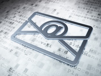 Ein silberner Briefumschlag mit dem E-Mail-@-Zeichen liegt auf einem Dokument
